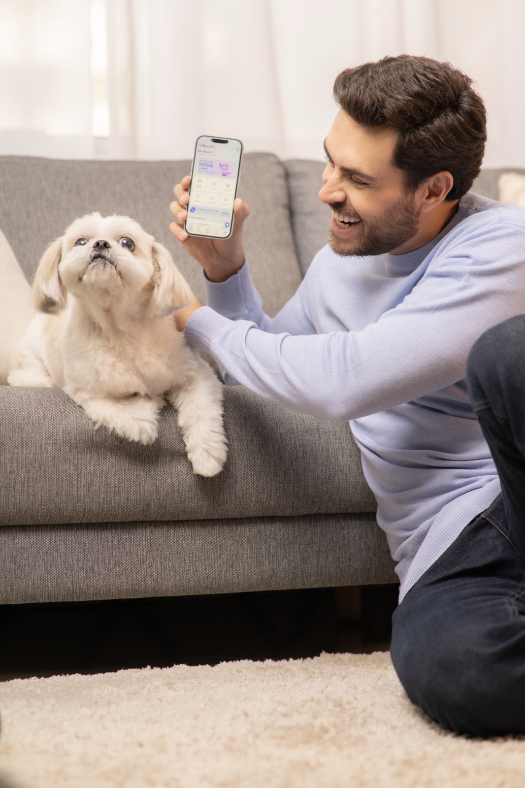 Homem sorrindo com o app vida.com no celular, ao lado do cachorro no sofá